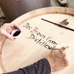 Painting the name Doc Brown Farm & Distillers onto an oak barrel