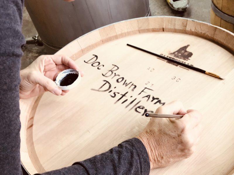 Painting the name Doc Brown Farm & Distillers onto an oak barrel